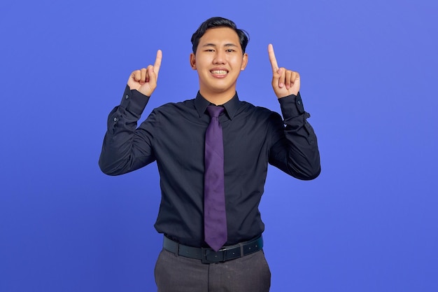 Retrato de um jovem asiático alegre apontando para a promoção de anúncios diretos em fundo roxo