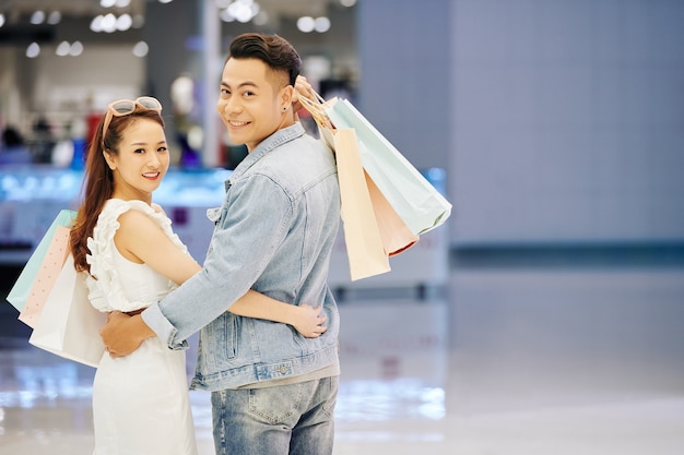 Retrato de um jovem asiático alegre e mulheres segurando sacolas de compras, se abraçando e se virando para sorrir