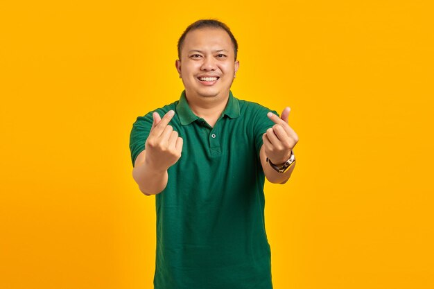 Retrato de um jovem asiático alegre mostrando o coração do dedo sobre fundo amarelo
