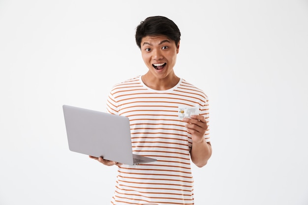 Retrato de um jovem asiático animado segurando um laptop