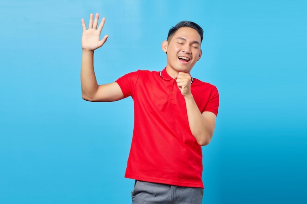 Retrato de um jovem asiático atraente de camisa vermelha cantando alto enquanto estava isolado em fundo azul