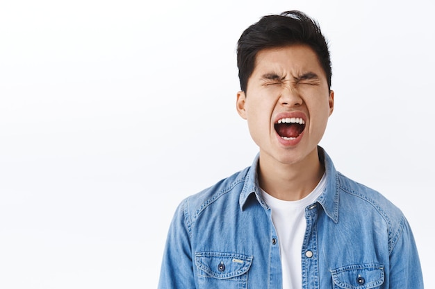 Retrato de um jovem asiático bobo chorando como um bebê, chorando e gritando, reclamando da vida cruel e injusta, fecha os olhos e grita incomodado, deprimido