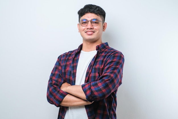 Retrato de um jovem asiático bonito vestindo camisa casual e óculos de pé com os braços cruzados e sorrindo para a câmera