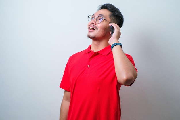 Retrato de um jovem asiático bonito vestindo camisa casual e óculos rindo ao fazer uma ligação