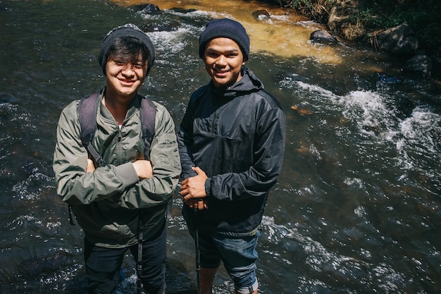 Retrato de um jovem asiático confiante com uma jaqueta de pára-quedas sorrindo enquanto está de pé em um rio