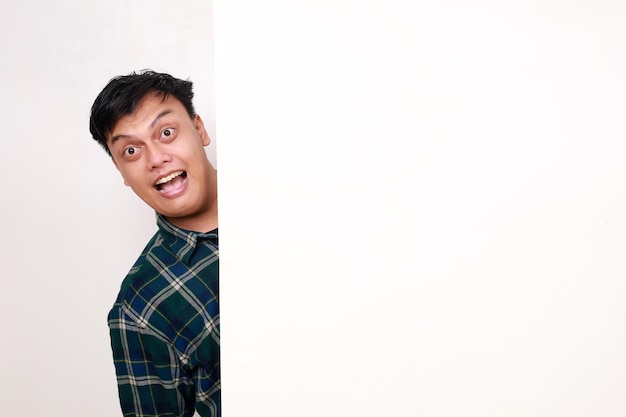 Retrato de um jovem asiático de pé atrás de um cartaz vazio com expressão facial feliz