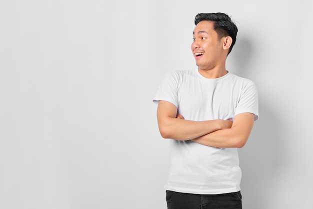 Retrato de um jovem asiático espantado cruzou os braços e olhando de lado para o espaço em branco isolado no fundo branco