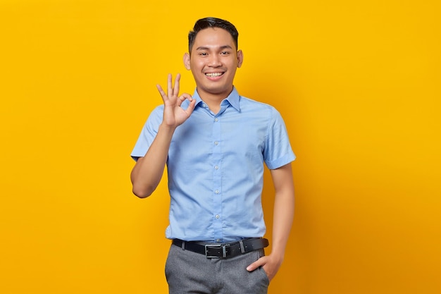 Retrato de um jovem asiático sorridente em óculos mostrando sinal bem isolado no conceito de empresário e empresário de fundo amarelo