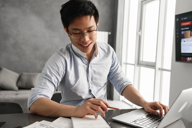 Retrato de um jovem asiático sorridente, usando o computador portátil