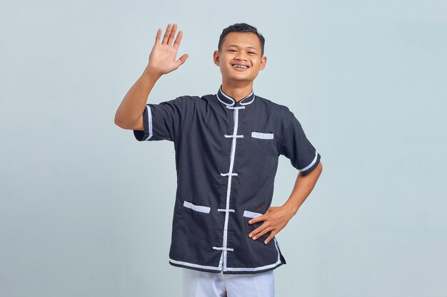 Retrato de um jovem asiático sorrindo com quimono de taekwondo fazendo um gesto com as palmas das mãos