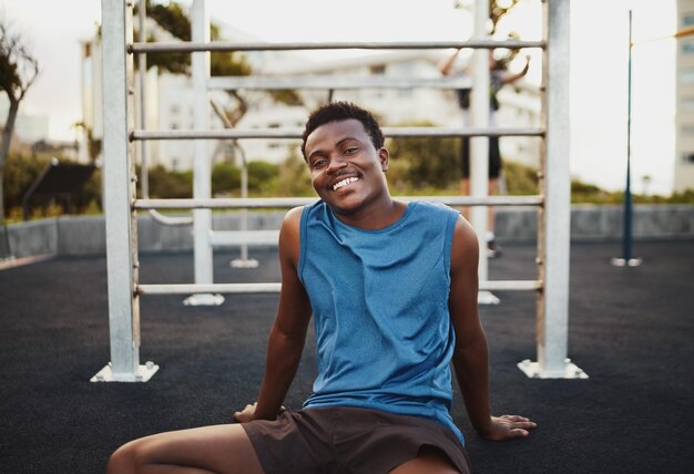 Retrato de um jovem atleta afro-americano sorridente relaxando depois de um treino intenso no parque de ginástica ao ar livre