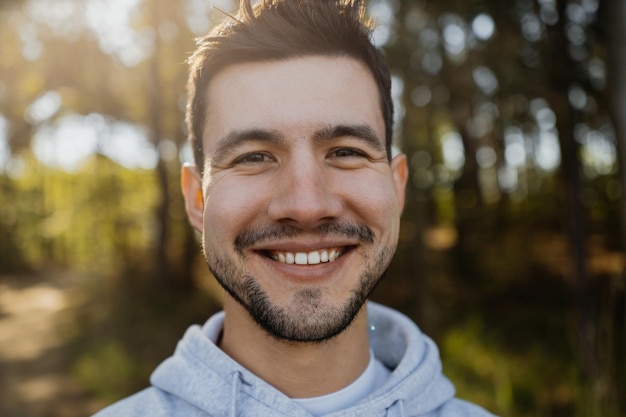 Foto retrato de um jovem atraente malhando sorrindo e posando para a câmera na floresta vestido com