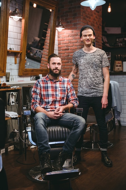 Retrato de um jovem barbeiro moderno e seu cliente barbudo de conteúdo atraente na barbearia