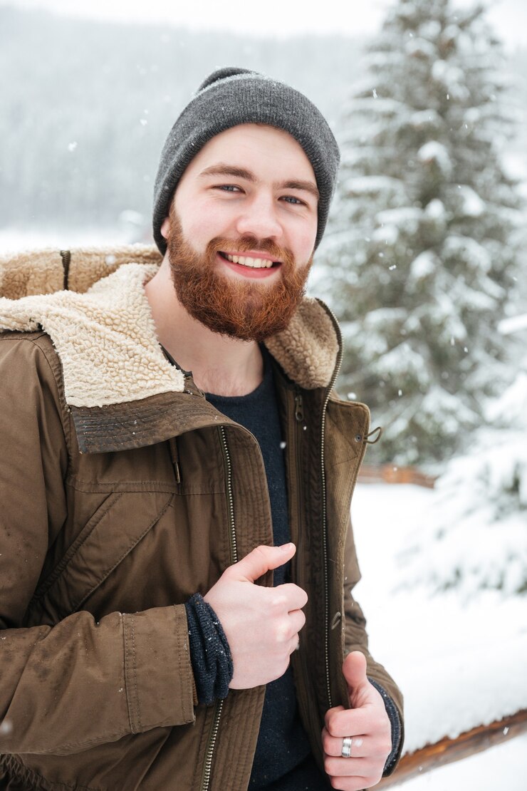 Foto retrato de um jovem barbudo bonito e alegre em pé na floresta de inverno
