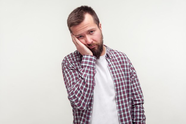 Retrato de um jovem barbudo entediado em camisa xadrez, inclinando-se por lado com expressão de rosto preguiçoso maçante, olhar indiferente deprimido cansado de tudo o tiro de estúdio interno isolado no fundo branco