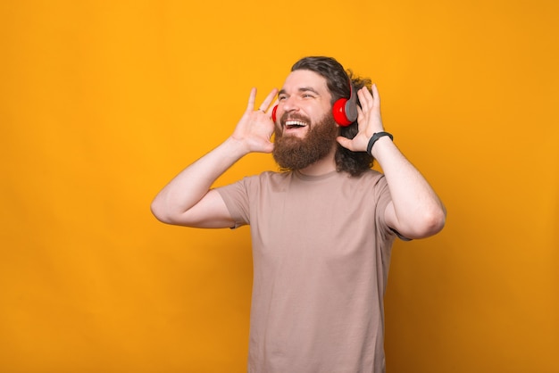 Retrato de um jovem barbudo hippie ouvindo música em fones de ouvido vermelhos sobre amarelo
