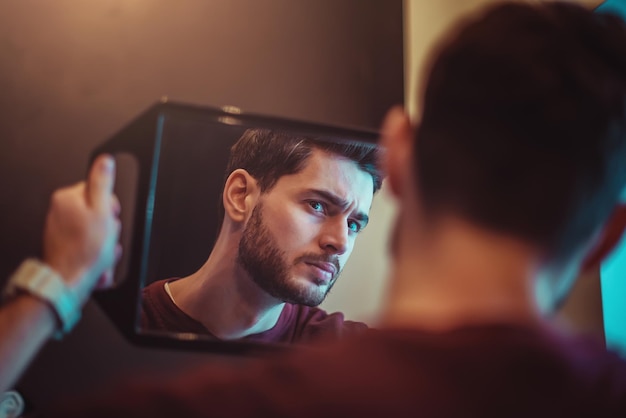 Retrato de um jovem barbudo que se olha através do espelho no salão de beleza.