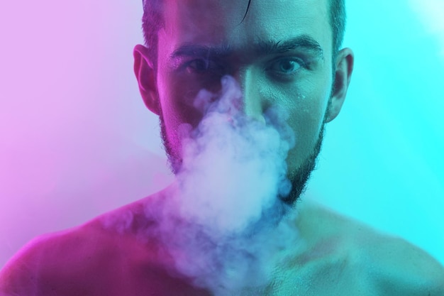 Retrato de um jovem bonito com pele molhada em vape de fumo de luz ultravioleta