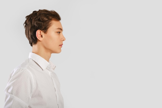 Foto retrato de um jovem bonito de camisa branca sobre fundo de estúdio cinza no perfil