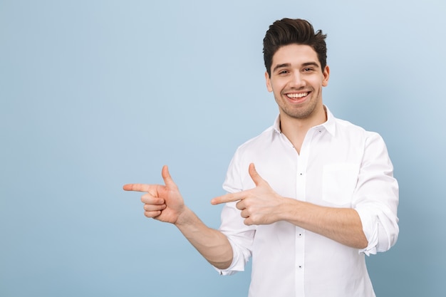 Retrato de um jovem bonito e alegre, isolado em um azul, apontando para o espaço da cópia