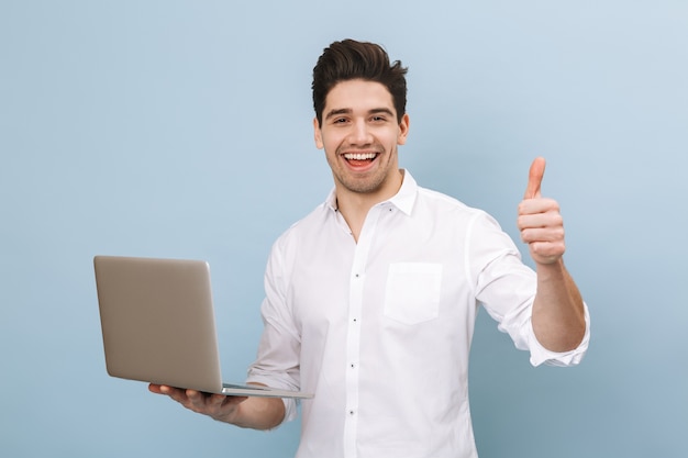 Retrato de um jovem bonito e alegre, isolado em uma azul, trabalhando em um laptop