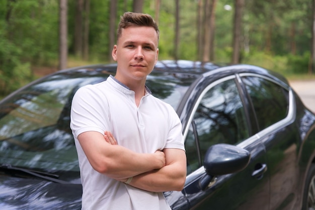 Retrato de um jovem bonito e feliz, um cara positivo parado perto de seu carro sorrindo olhando para a câmera