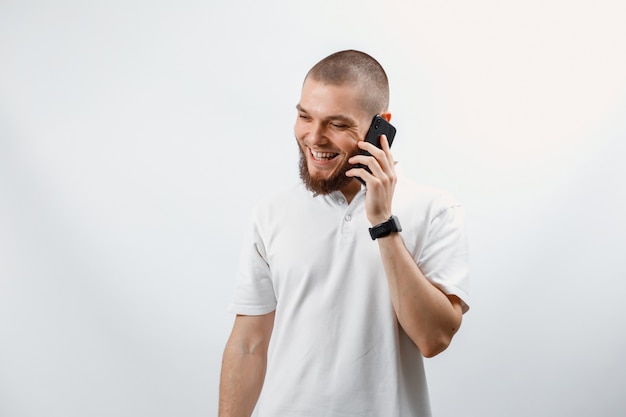 Retrato de um jovem bonito em uma camiseta branca falando no smartphone em branco