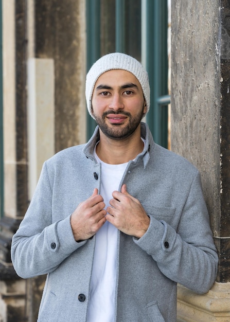 Foto retrato de um jovem bonito homem asiático sorridente com uma barba arrumada vestindo um casaco leve e um chapéu de tricô branco