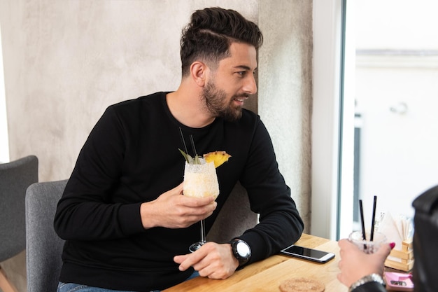 Retrato de um jovem bonito sentado no restaurante e bebendo coquetel frio e colada