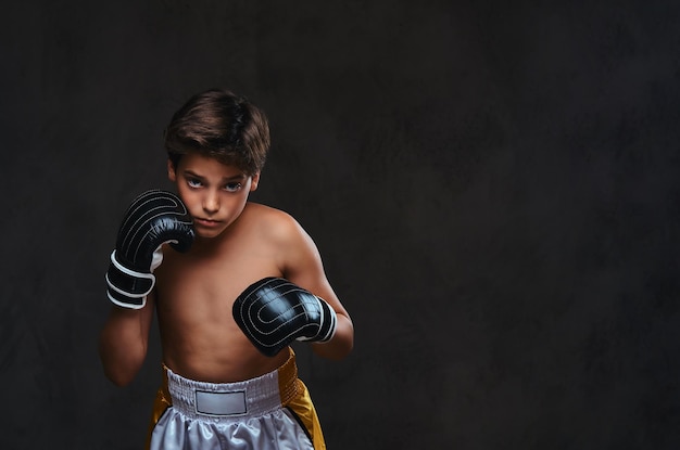 Retrato de um jovem boxeador sem camisa bonito usando luvas, olhando para uma câmera. Isolado no fundo escuro.