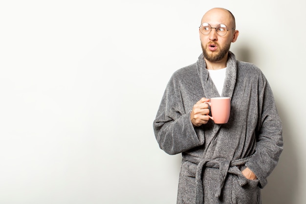 Retrato de um jovem careca com uma barba em um roupão e óculos, segurando uma xícara de café