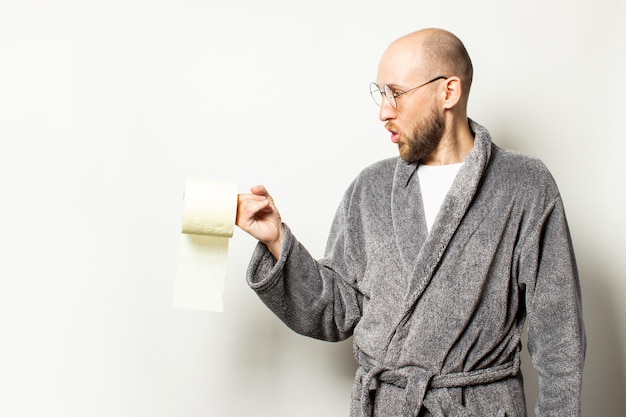 Retrato de um jovem careca com uma barba em um roupão e óculos tem papel higiênico na mão