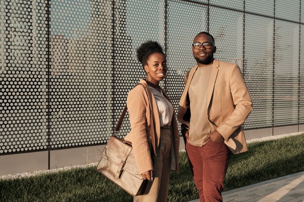 Retrato de um jovem casal africano em ternos elegantes, sorrindo para a câmera em pé na cidade