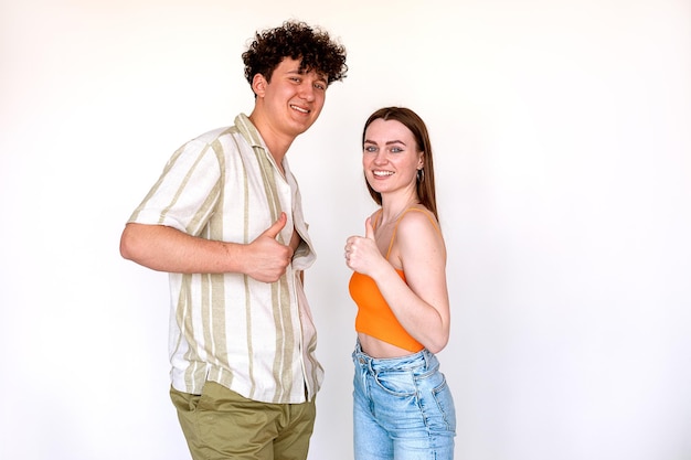 Retrato de um jovem casal alegre posando em fundo branco jovem homem sorridente e encaracolado e mulher mostrando sinal de polegar para cima