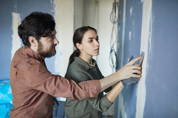 Foto retrato de um jovem casal alisando a parede seca da cintura para cima durante a reforma da casa, copie o espaço