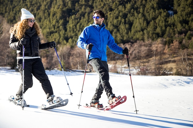 Retrato de um jovem casal andando em raquetes de neve sobre fundo de inverno.