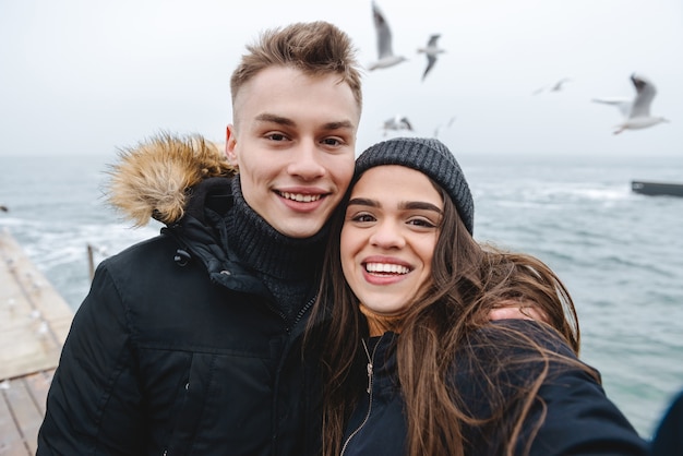 retrato de um jovem casal apaixonado, caminhando na praia ao ar livre, se divertindo, tire uma selfie pela câmera.