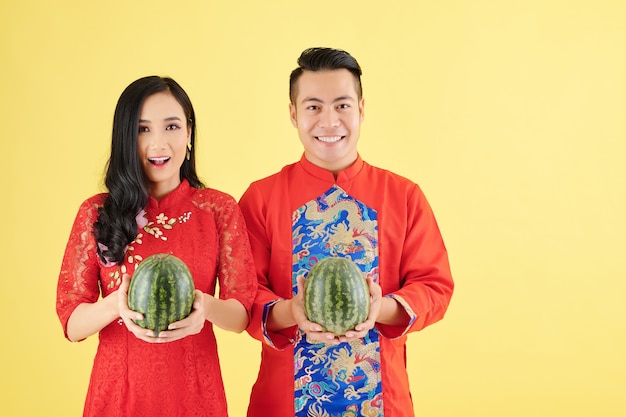 Retrato de um jovem casal asiático feliz em trajes tradicionais de Ano Novo Lunar segurando melancias maduras