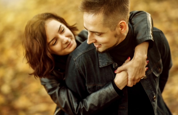 Retrato de um jovem casal de amantes abraçados em um fundo embaçado de folhas de outono caídas no parque.