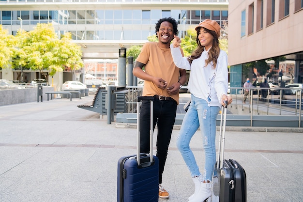 Retrato de um jovem casal de turistas carregando uma mala em pé do lado de fora do aeroporto ou da estação de trem