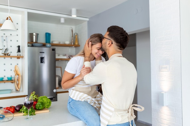 Retrato de um jovem casal feliz cozinhando juntos na cozinha em casa romântico Jovem atraente e homem bonito estão gostando de passar tempo juntos em pé na cozinha moderna leve