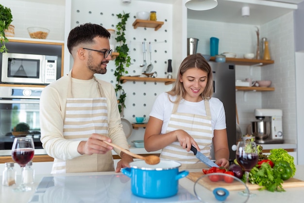 Retrato de um jovem casal feliz cozinhando juntos na cozinha em casa romântico jovem atraente e homem bonito estão gostando de passar tempo juntos em pé na cozinha moderna leve