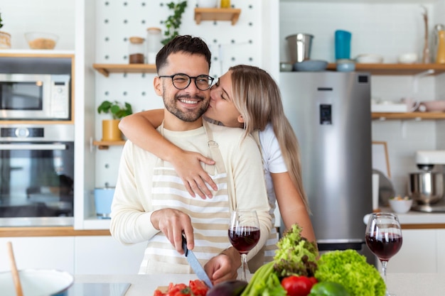 Retrato de um jovem casal feliz cozinhando juntos na cozinha em casa romântico jovem atraente e homem bonito estão gostando de passar tempo juntos em pé na cozinha moderna leve