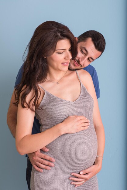 Retrato de um jovem casal feliz, homem segurando a barriga de sua esposa grávida isolado sobre fundo azul