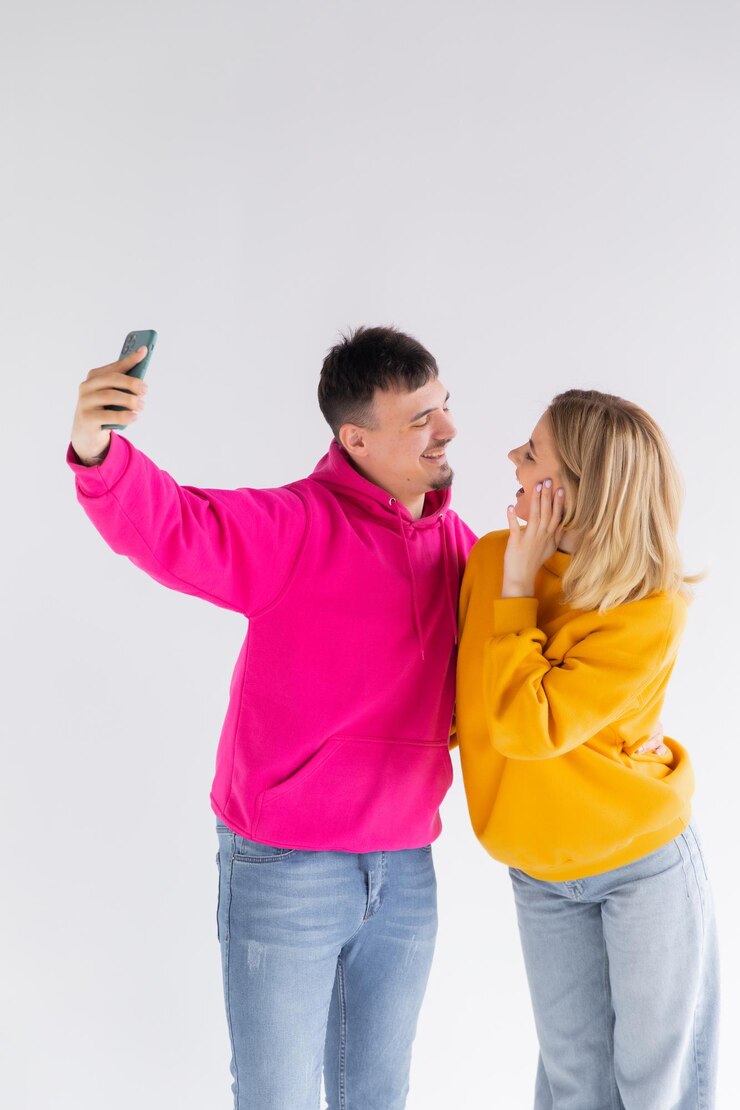 Foto retrato de um jovem casal feliz, mostrando os polegares enquanto tirava uma selfie juntos
