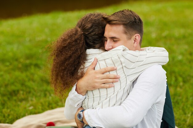 Foto retrato de um jovem casal feliz se abraçando enquanto está sentado na grama verde durante um encontro romântico ao ar livre