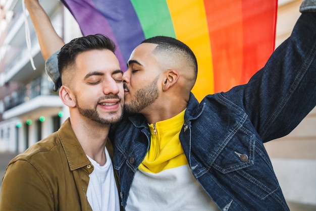 Foto retrato de um jovem casal gay abraçando e mostrando seu amor com a bandeira do arco-íris na rua. lgbt e conceito de amor.