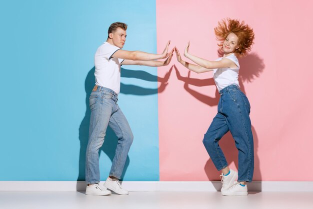 Retrato de um jovem casal lindo dançando alegremente isolado sobre o fundo rosa azul do estúdio