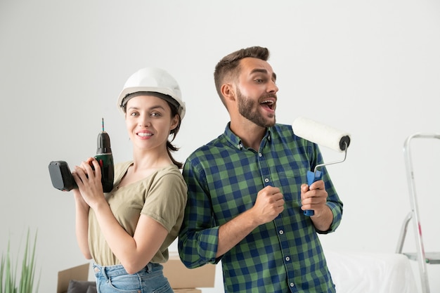 Foto retrato de um jovem casal positivo levantando ferramentas de remodelação enquanto está pronto para conserto em um novo apartamento