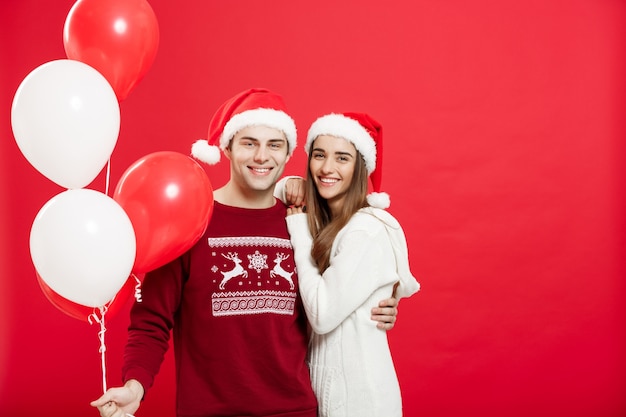 Retrato de um jovem casal romântico com balão de natal sobre o fundo do estúdio vermelho.